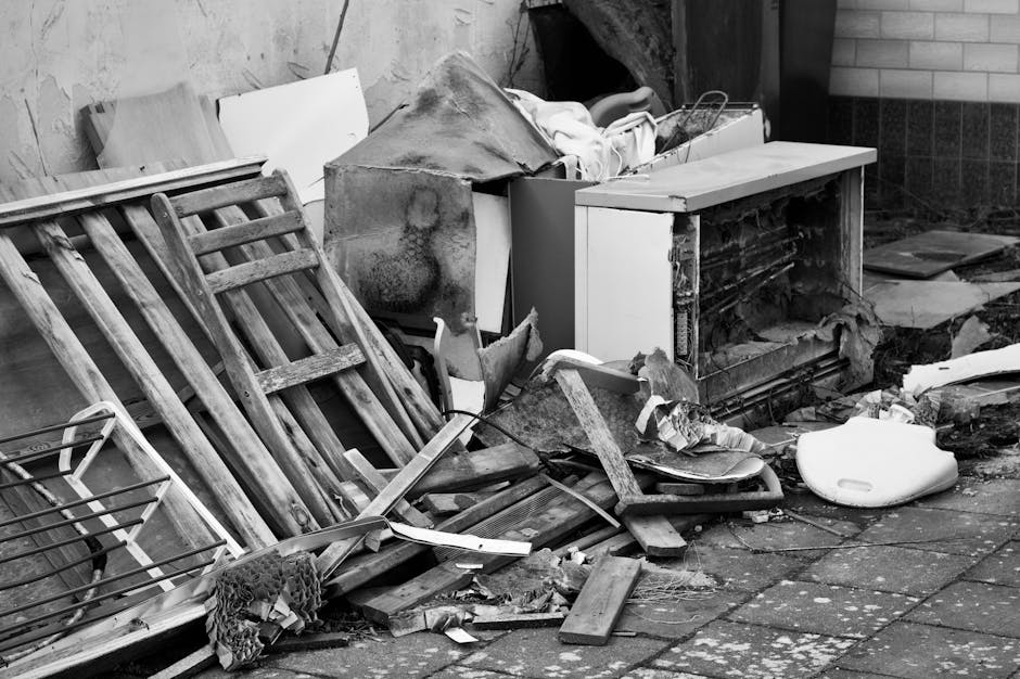 A pile of mixed household rubbish and waste materials is scattered on the ground, including black plastic bags, a yellow plastic storage container, a discarded car tire, and various small debris. The